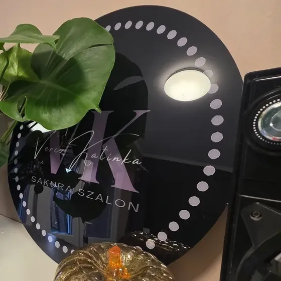 A szalon kerek, fekete cégtáblája lila-arany monogrammal, rajta a Vercz Katinka és a Sakura Szalon felirat.